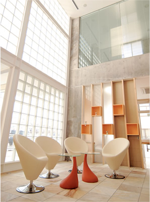 モダンな歯科クリニックの待合室の写真。低いアングルから見上げた構図で、光が差し込む大きなガラスブロックの壁と、白い椅子が配されたシンプルな空間です。