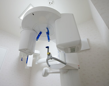 真っ白な部屋の中央に歯科用CTが配置されている写真。撮影時には、頭部を固定することで、3次元画像を撮影できるX線装置。